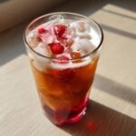 Close-up of a tall glass filled with Iced Raspberry Vanilla Chai, ice cubes, and fresh raspberries.