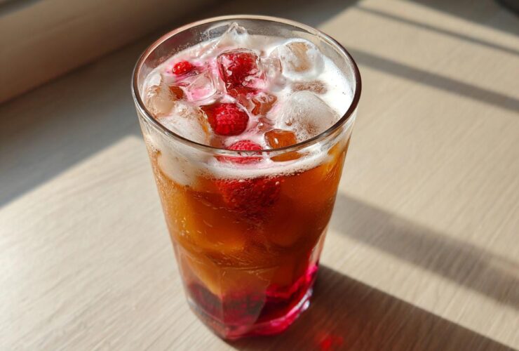 Close-up of a tall glass filled with Iced Raspberry Vanilla Chai, ice cubes, and fresh raspberries.