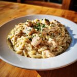 A white bowl filled with creamy Instant Pot Creamy Chicken and Orzo, topped with diced chicken and fresh parsley.