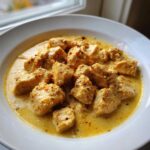Close-up of tender chicken pieces in a rich, yellow Instant Pot Creamy Coconut Chicken Curry sauce, topped with chili flakes.