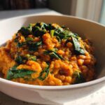 A close-up of Instant Pot Creamy Coconut Lentils with Spinach served in a white bowl, featuring orange lentils and wilted green spinach.