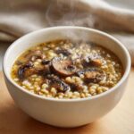 Close-up of a steaming bowl of Instant Pot Creamy Mushroom Barley Soup, featuring plump barley and sliced mushrooms.