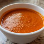 Close-up of a white bowl filled with rich, orange-red Instant Pot Creamy Red Pepper Tomato Soup.