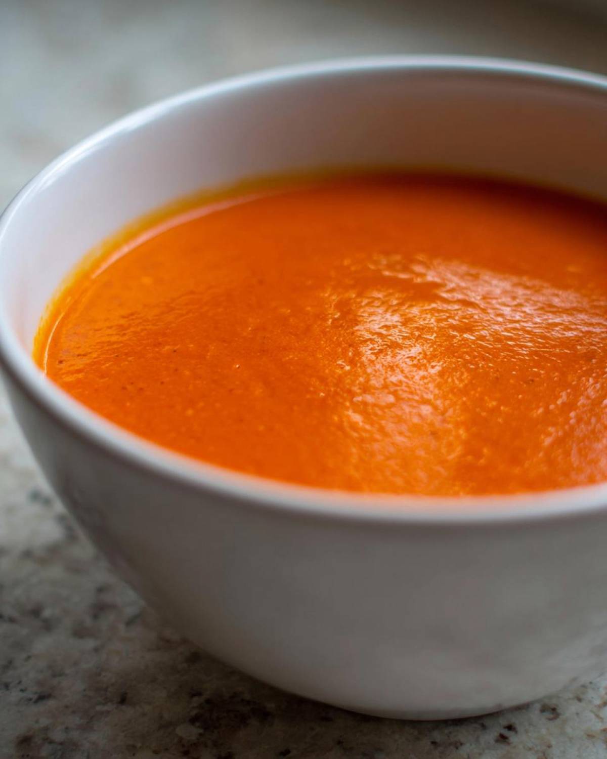 Close-up of vibrant orange Instant Pot Creamy Red Pepper Tomato Soup served in a white bowl.