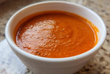 Close-up of a white bowl filled with rich, orange-red Instant Pot Creamy Red Pepper Tomato Soup.