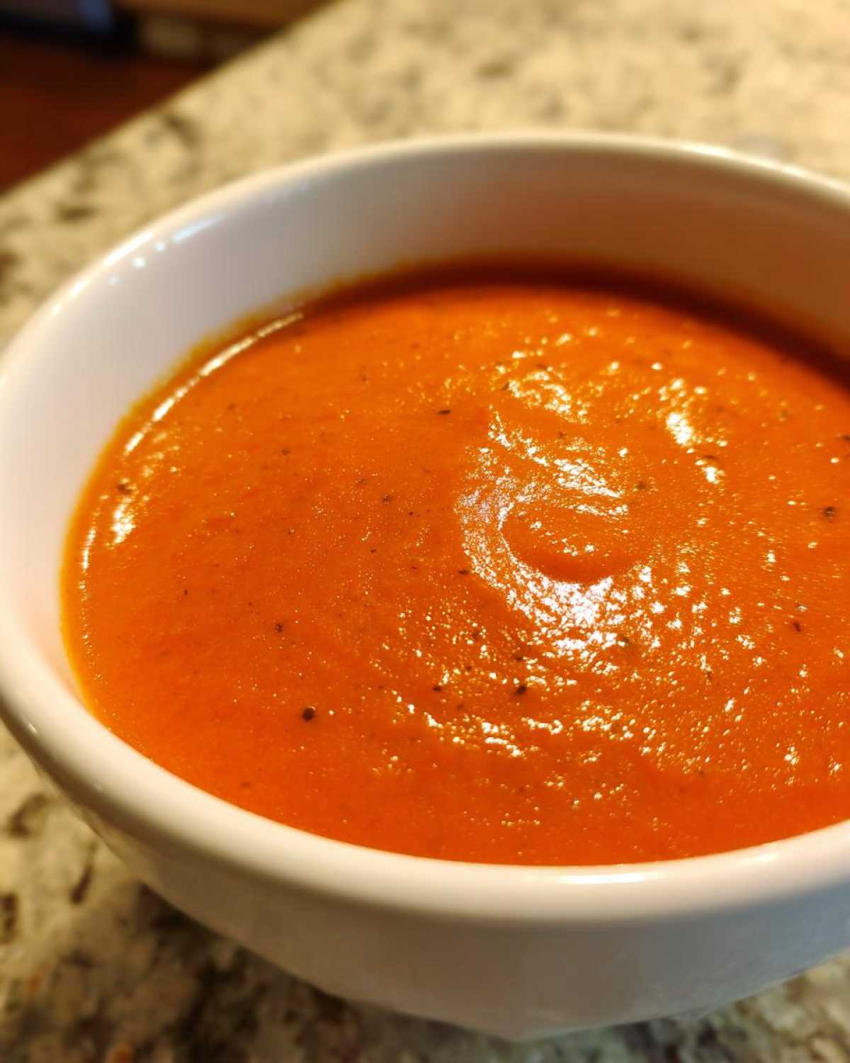 A close-up shot of rich, vibrant orange Instant Pot Creamy Red Pepper Tomato Soup in a white bowl.