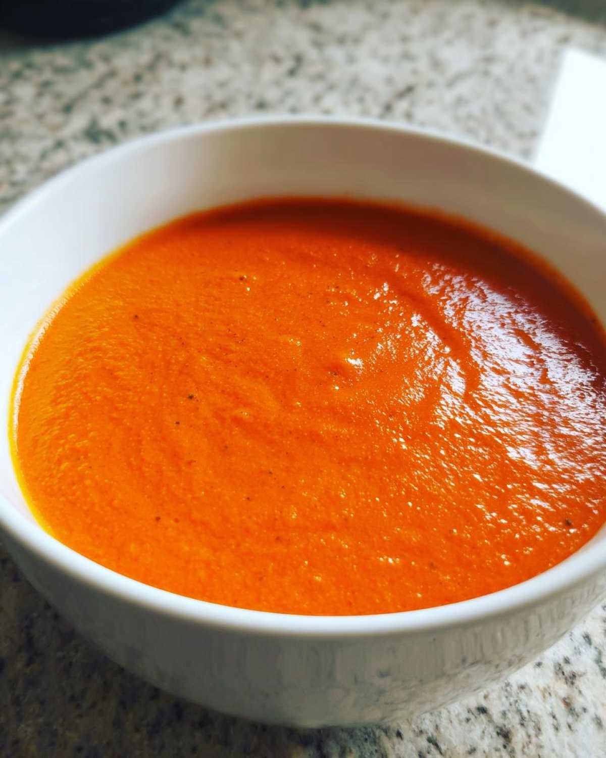 Close-up of a white bowl filled with vibrant orange Instant Pot Creamy Red Pepper Tomato Soup.