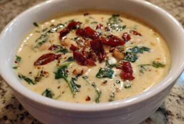 A close-up of a white bowl filled with Instant Pot Creamy Tuscan White Bean Soup, topped with sun-dried tomatoes and spinach.