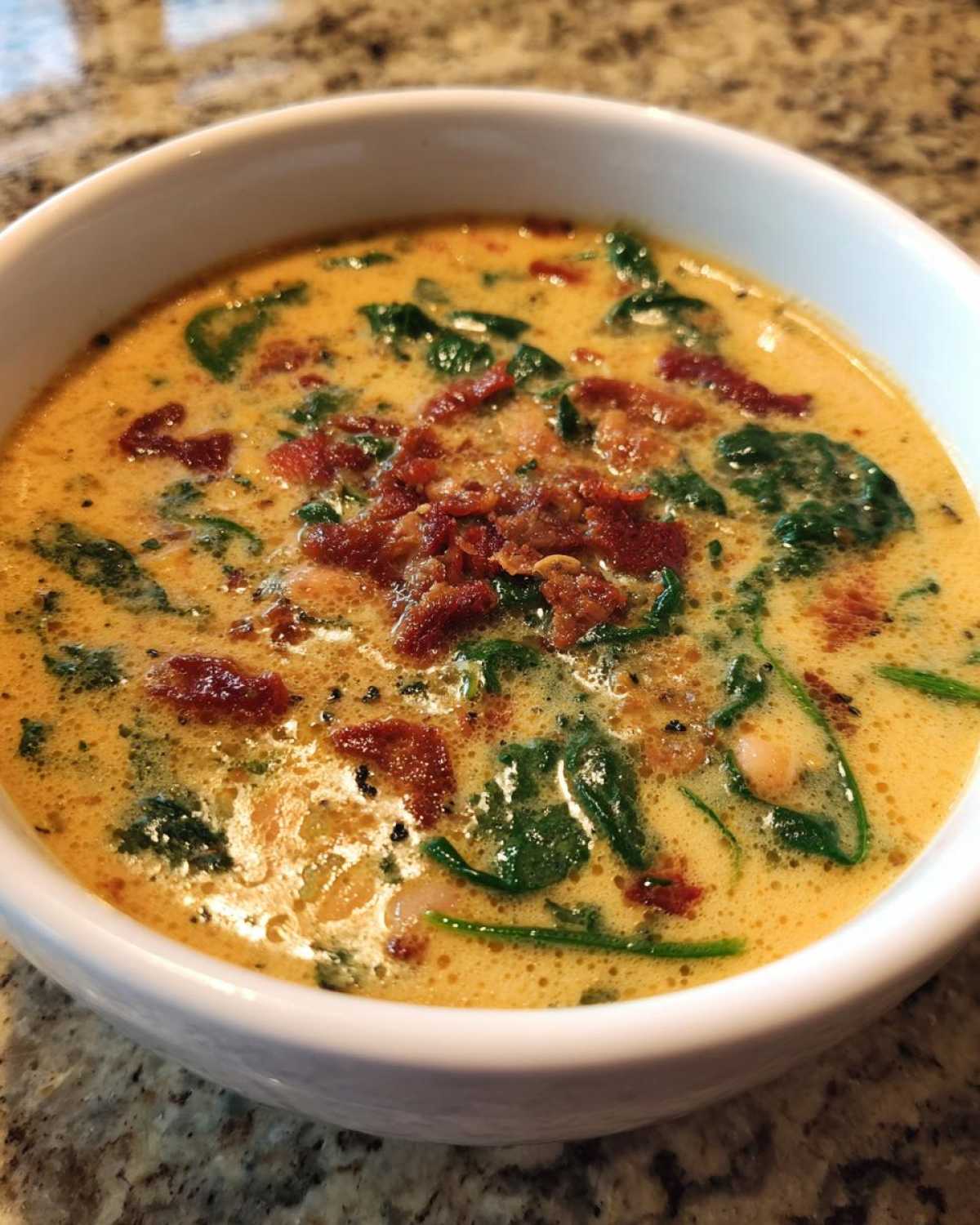 Close-up of a white bowl filled with Instant Pot Creamy Tuscan White Bean Soup, topped with bacon bits and spinach.