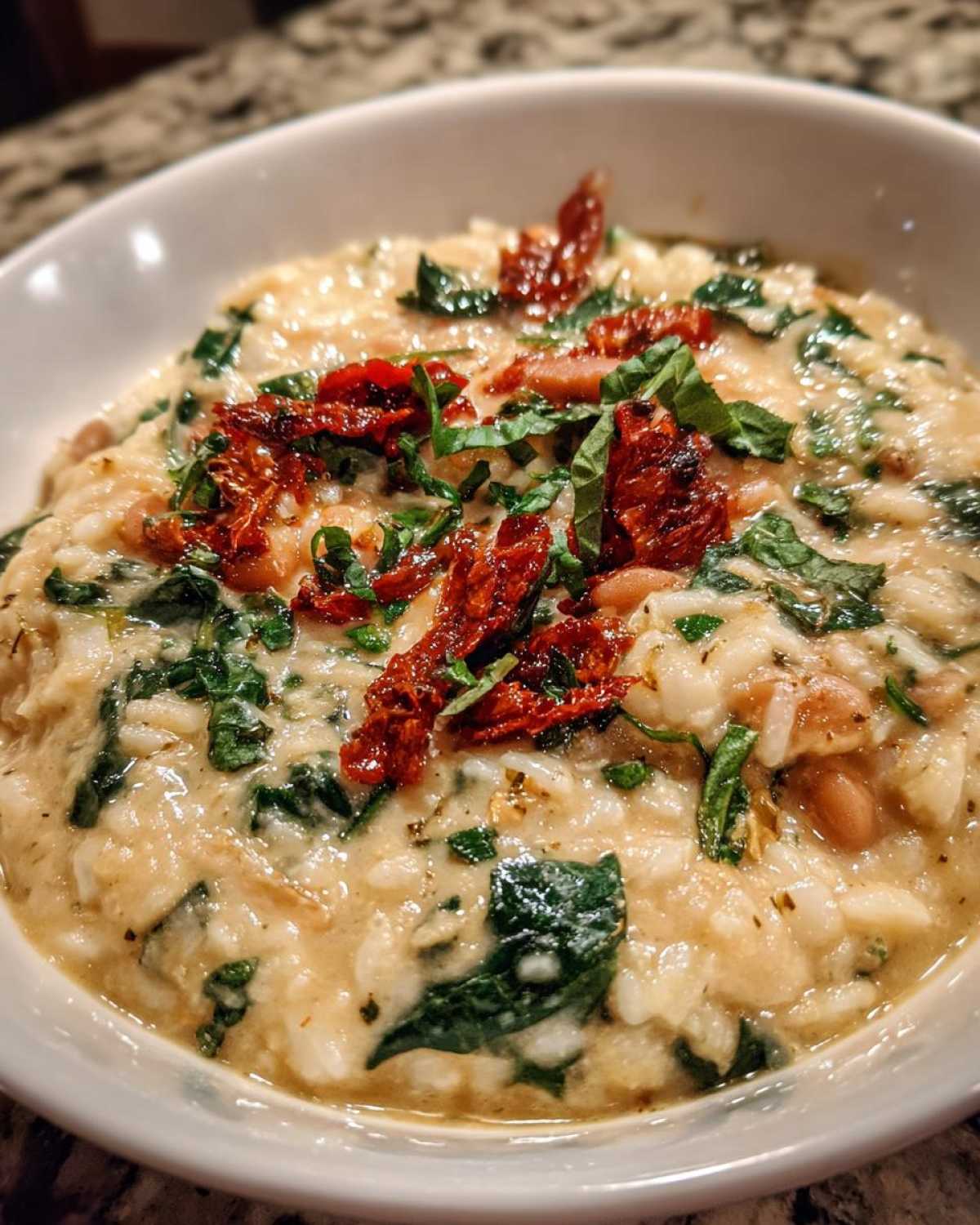 A close-up of Instant Pot Creamy Tuscan White Bean Soup, showing creamy rice, beans, spinach, and sun-dried tomatoes.