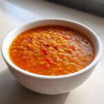 Close-up of rich, orange Instant Pot Tomato Lentil Soup served in a white bowl.