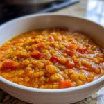 A close-up of a white bowl filled with thick, vibrant orange Instant Pot Tomato Lentil Soup, showing cooked lentils and diced vegetables.
