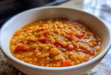 A close-up of a white bowl filled with thick, vibrant orange Instant Pot Tomato Lentil Soup, showing cooked lentils and diced vegetables.