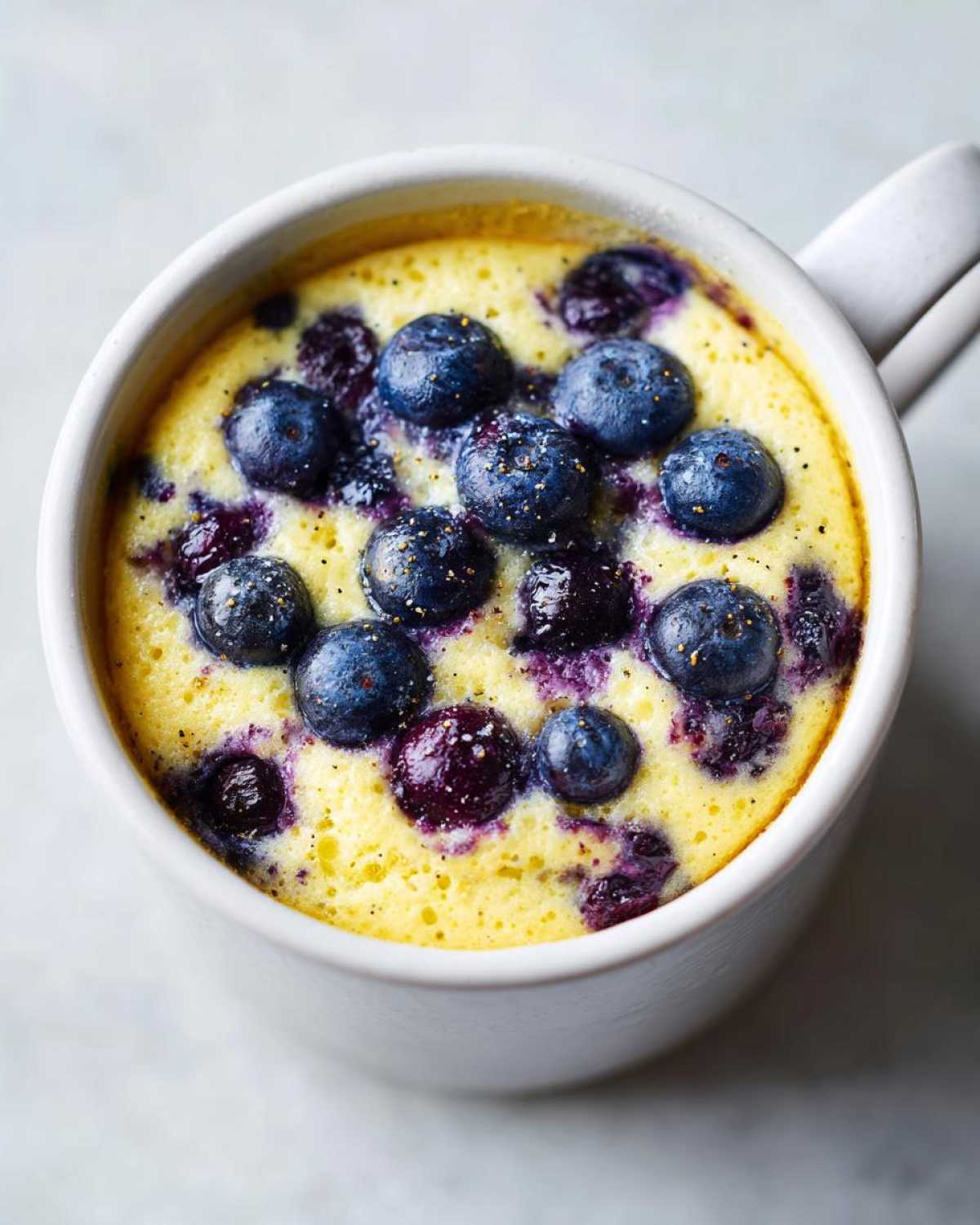 Close-up of a freshly baked Keto Blueberry Lemon Mug Cake topped with whole blueberries.