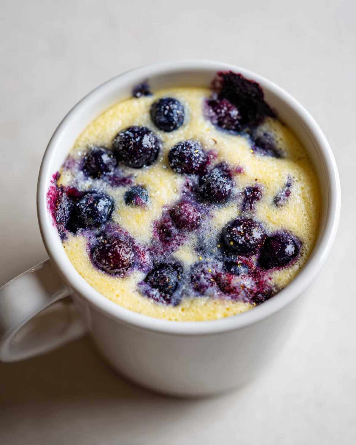 Close-up of a warm Keto Blueberry Lemon Mug Cake topped with plump blueberries.