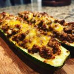 Two halves of baked zucchini boats stuffed with seasoned ground meat and melted cheddar cheese, ready to eat as Keto Cheesy Taco Stuffed Zucchini Boats.