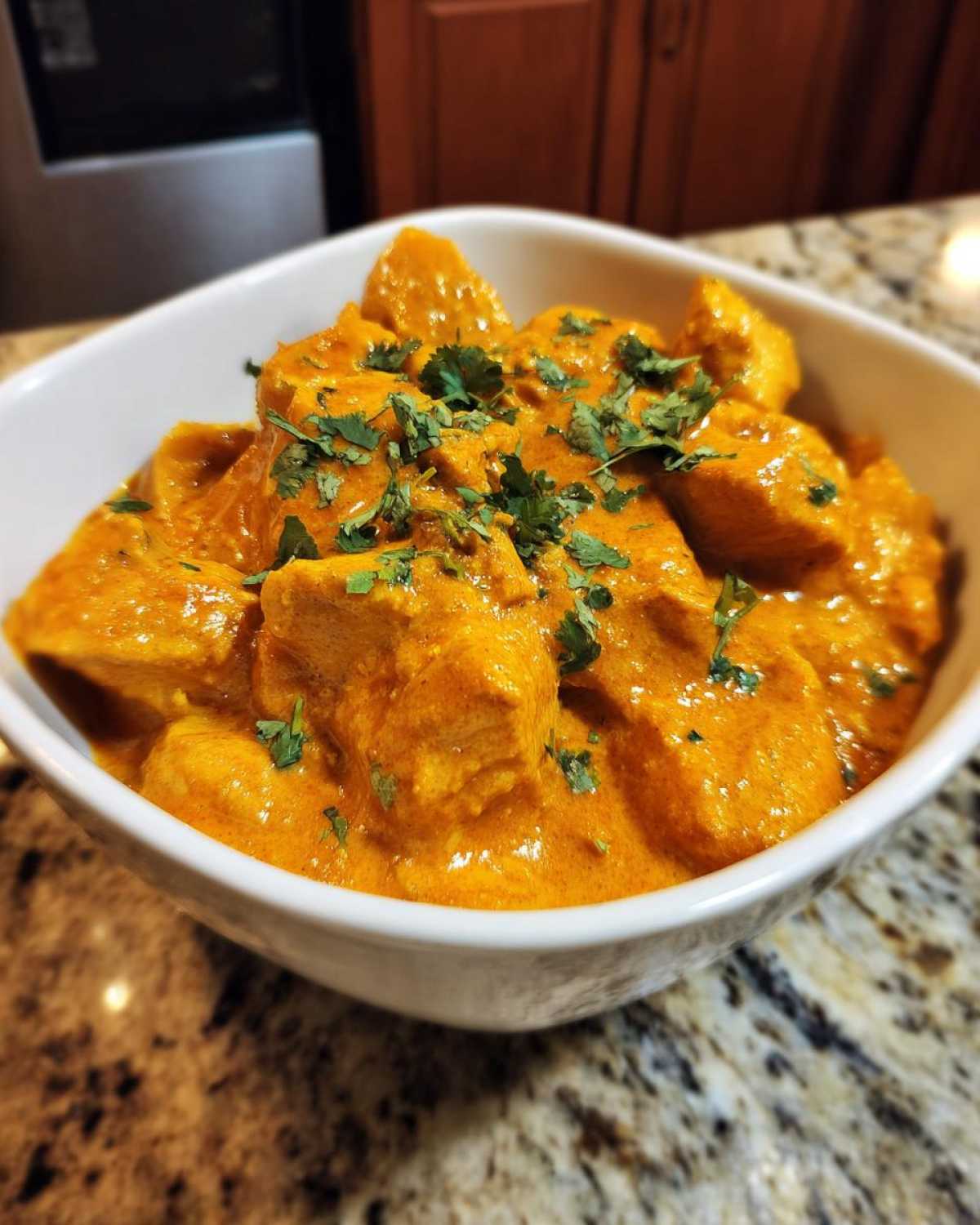 A white bowl filled with rich, orange Keto Creamy Butter Chicken Skillet, garnished with fresh cilantro.