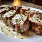 Close-up of sliced Keto Creamy Garlic Herb Pork Tenderloin drizzled generously with a rich, herb-flecked cream sauce.