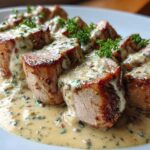 Slices of seared pork tenderloin covered in a rich Keto Creamy Garlic Herb sauce and garnished with parsley.