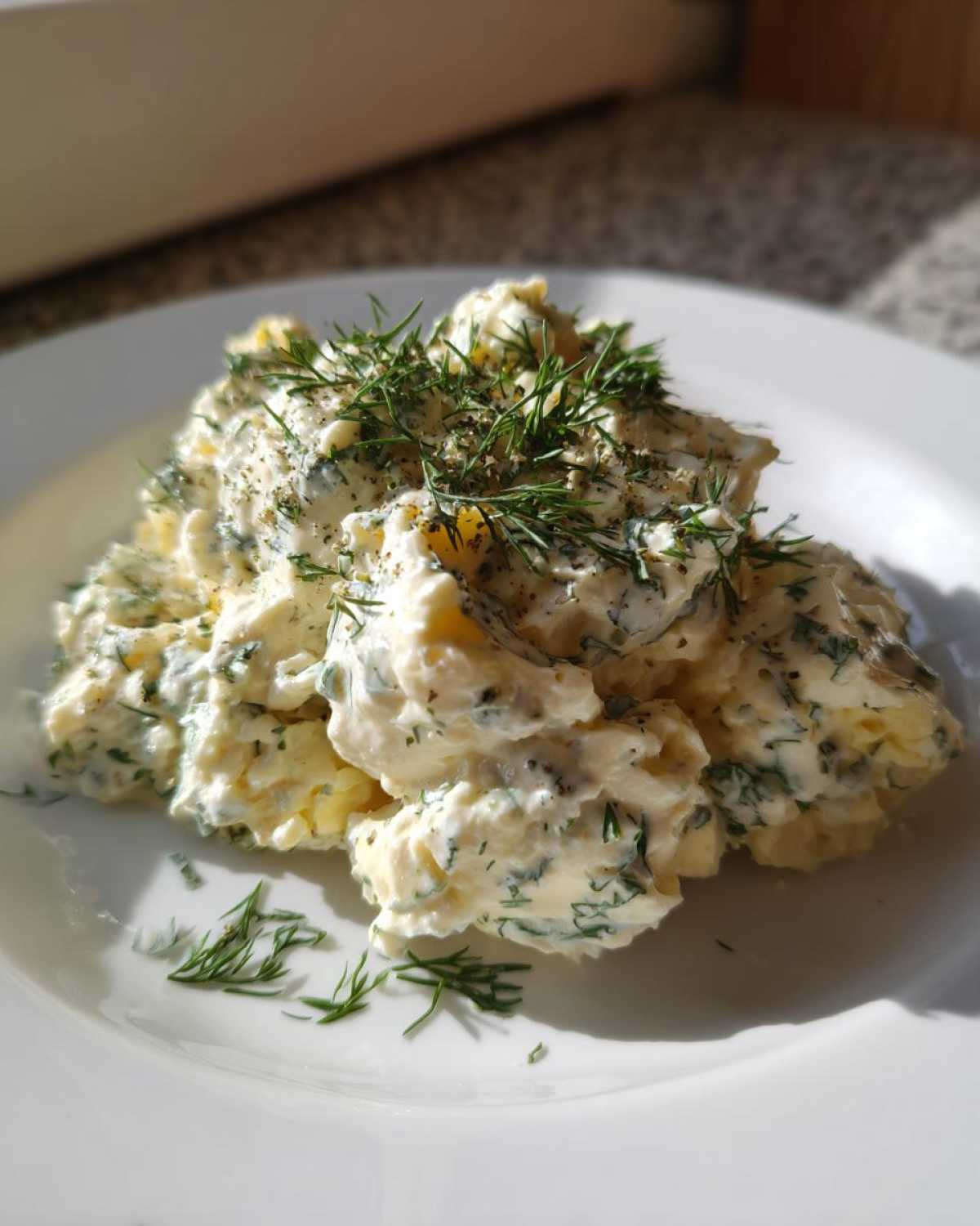 A mound of Keto Creamy Herb Deviled Egg Salad topped with fresh dill and pepper on a white plate.