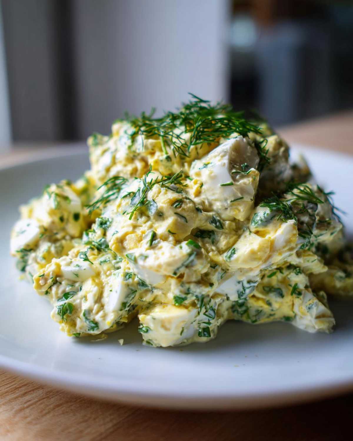 A mound of Keto Creamy Herb Deviled Egg Salad topped with fresh dill on a white plate.