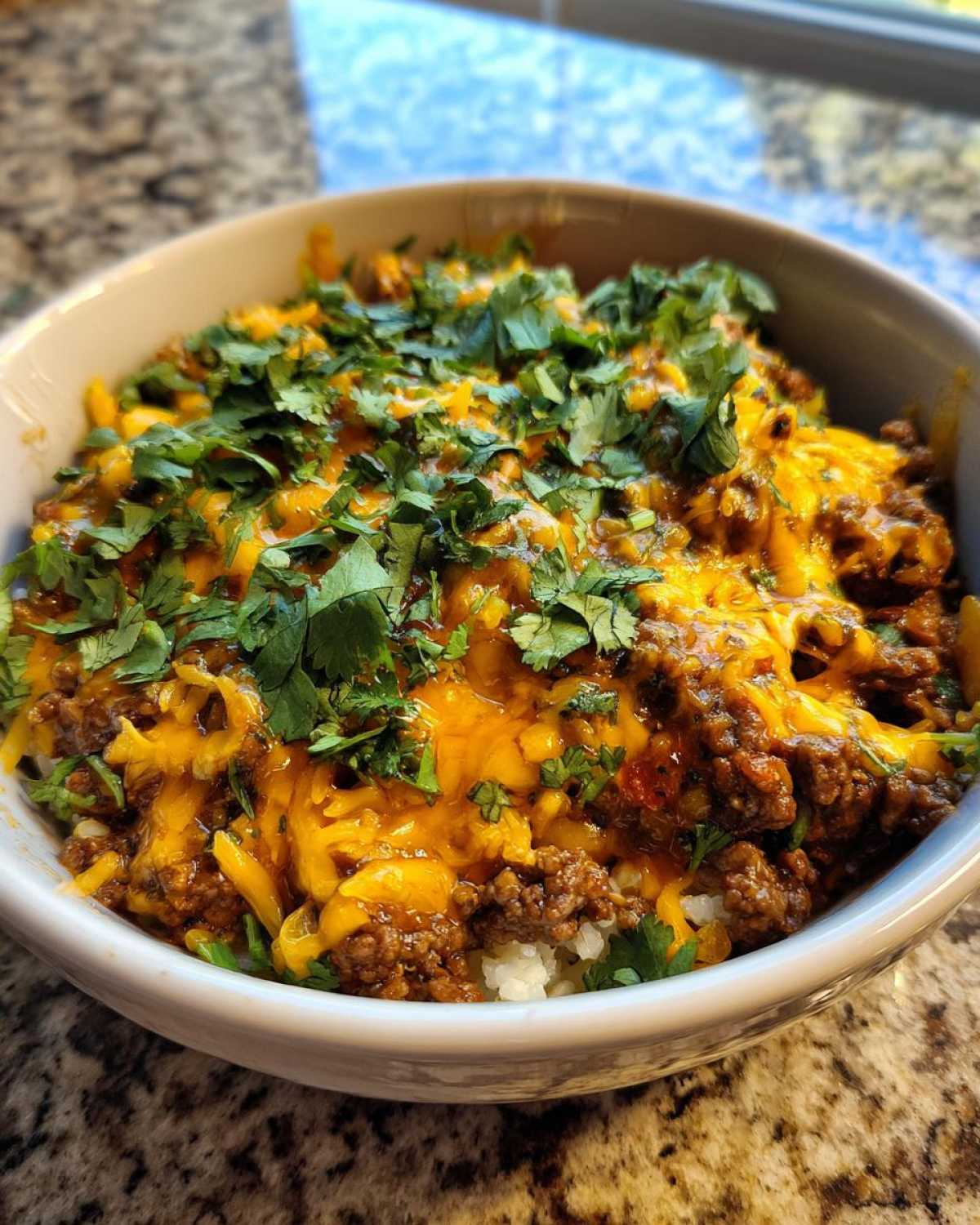 A close-up of a bowl filled with Keto Creamy Taco Skillet, featuring seasoned ground beef, melted cheddar cheese, and fresh cilantro over cauliflower rice.
