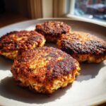 Four golden-brown, crispy Keto Crispy Cauliflower Hash Browns served on a light gray plate near a window.