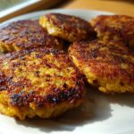 Five golden-brown, pan-fried Keto Crispy Cauliflower Hash Browns served on a light-colored plate.