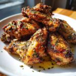 Close-up of golden brown Keto Crispy Parmesan Chicken Wings piled on a white plate, glistening with butter and sprinkled with parsley.
