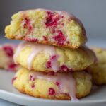 A stack of three soft Lemon Raspberry Cookies topped with a dripping pink glaze, one cookie broken open to show the interior.