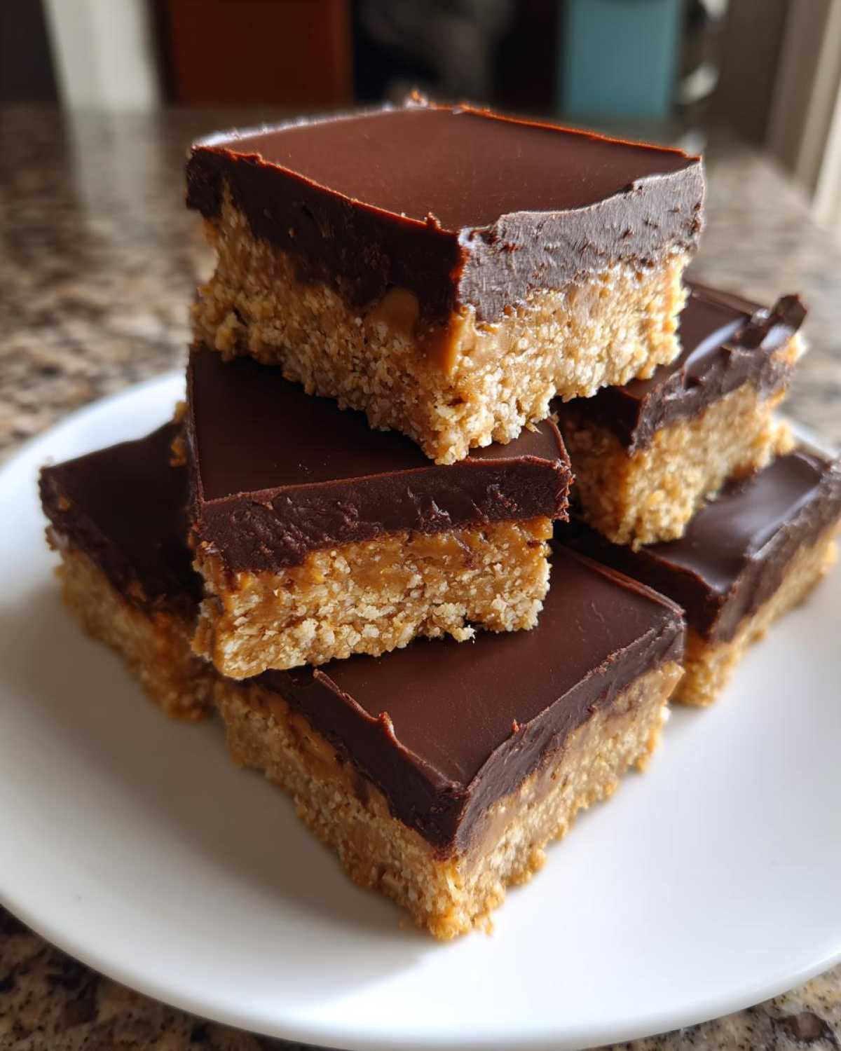 A stack of square Peanut Butter Bars featuring a thick, crumbly base and a smooth chocolate ganache topping.