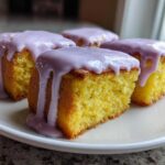 Four square Mini Lemon Cakes with Lavender Glaze stacked on a white plate, showing the moist yellow crumb.