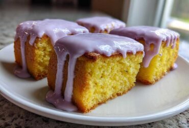 Four square Mini Lemon Cakes with Lavender Glaze stacked on a white plate, showing the moist yellow crumb.