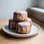 Four delicious Mini Lemon Cakes Lavender Glaze stacked on a small plate, drizzled with white icing and lemon zest.