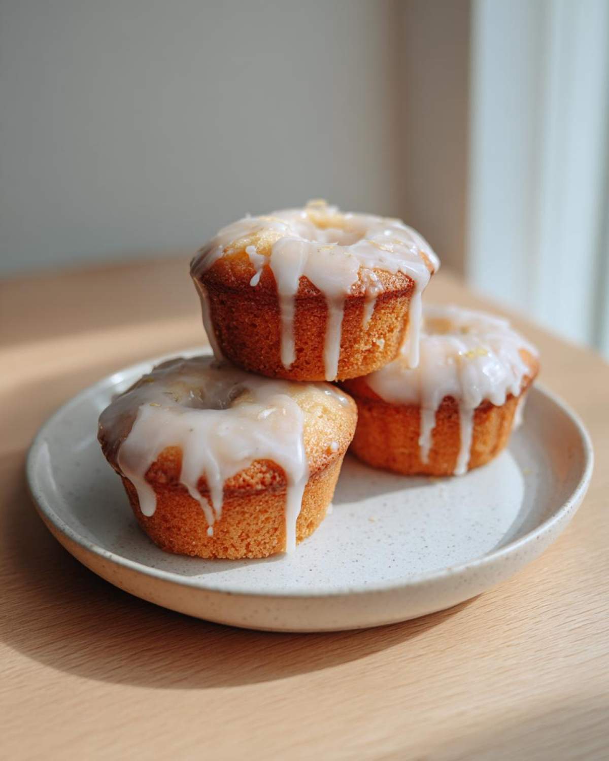 Three golden Mini Lemon Cakes Lavender Glaze stacked on a speckled white plate, drizzled with thick white icing.
