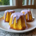 Three bright yellow Mini Lemon Cakes with Lavender Glaze drizzled on top, sitting on a white plate.