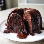 A slice cut from a moist Chocolate Bundt Cake, generously covered in dripping dark chocolate glaze.