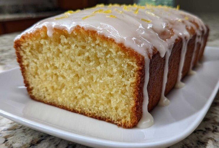 Close-up of a freshly baked, moist Lemon Loaf with thick white glaze dripping down the sides and topped with lemon zest.