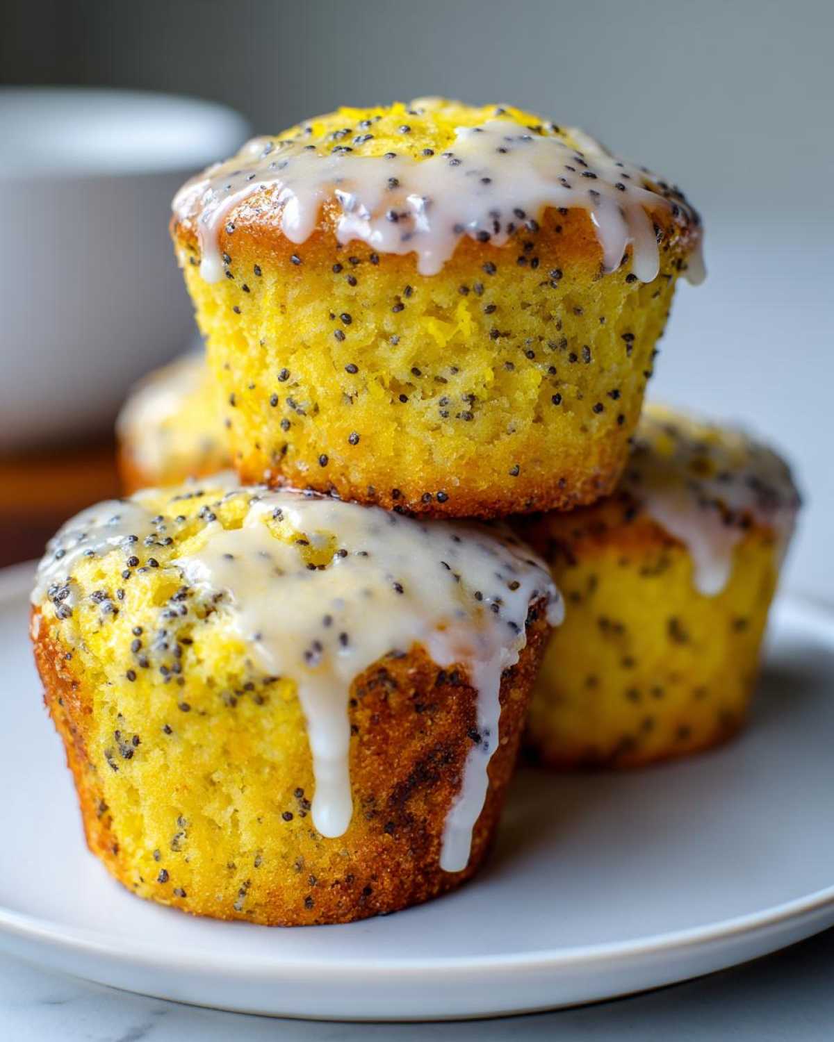 A stack of three moist Lemon Poppy Seed Muffins topped with a thick, dripping lemon glaze and visible poppy seeds.