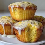 A stack of four moist Lemon Poppy Seed Muffins topped with a thick, dripping lemon glaze and visible poppy seeds.
