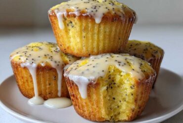 A stack of four moist Lemon Poppy Seed Muffins topped with a thick, dripping lemon glaze and visible poppy seeds.