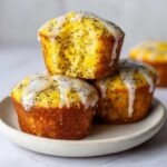 A stack of three moist Lemon Poppy Seed Muffins topped with a thick, dripping lemon glaze and poppy seeds.