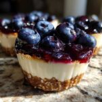 A close-up of a No-Bake Blueberry Cheesecake Oat Cup featuring a thick oat crust, creamy filling, and topped with blueberry compote and fresh blueberries.