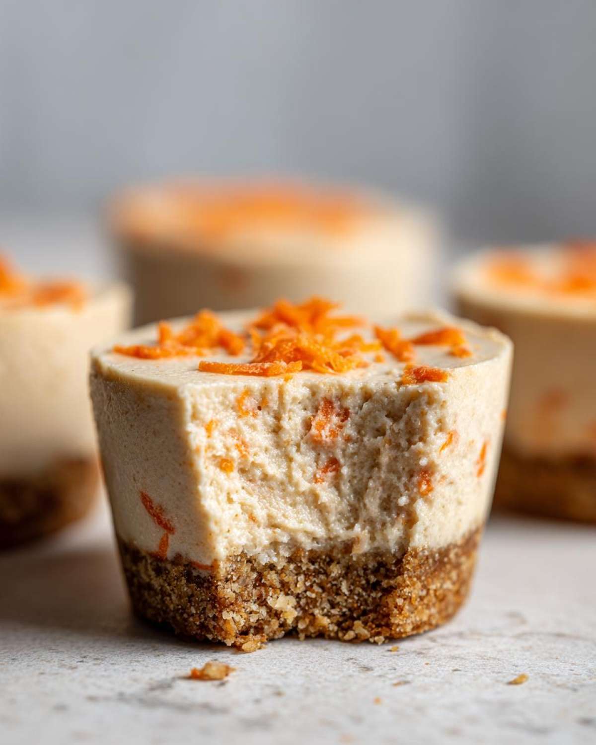 Close-up of a No-Bake Carrot Cake Cheesecake Cup with a bite taken out, showing creamy filling and crumb crust.