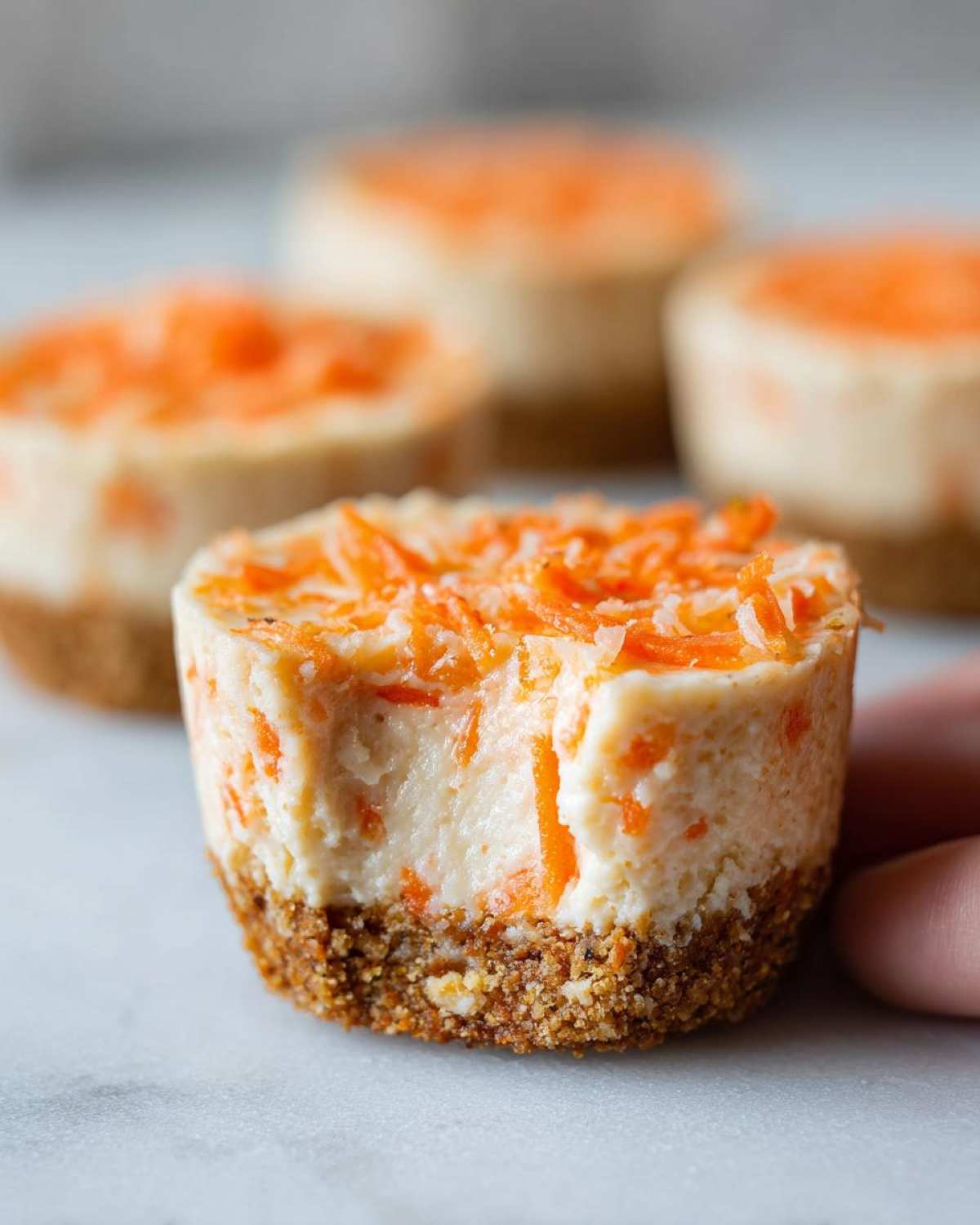 Close-up of a No-Bake Carrot Cake Cheesecake Cup with a bite taken out, showing creamy filling and graham cracker crust.