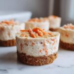 A single, perfectly formed No-Bake Carrot Cake Cheesecake Cup with a graham cracker crust, topped with shredded carrots.