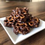 A pile of homemade No-Bake Chocolate Covered Pretzel Clusters sprinkled with sea salt on a white square plate.
