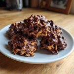 A stack of five No-Bake Chocolate Covered Pretzel Clusters coated in melted dark chocolate, resting on a small white plate.