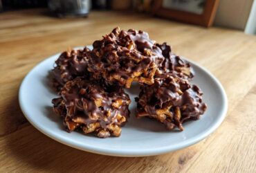 A stack of five No-Bake Chocolate Covered Pretzel Clusters coated in melted dark chocolate, resting on a small white plate.