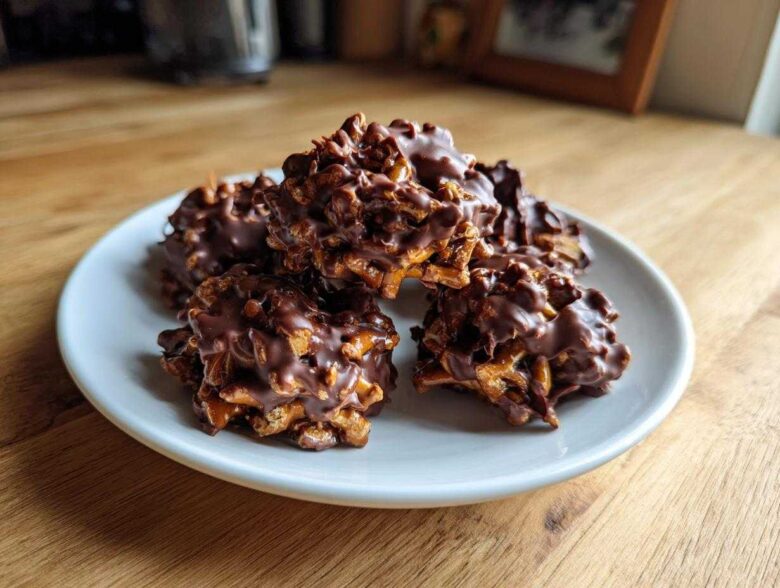 A stack of five No-Bake Chocolate Covered Pretzel Clusters coated in melted dark chocolate, resting on a small white plate.